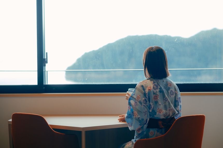 窓辺の椅子から海を眺める浴衣の女性の後ろ姿