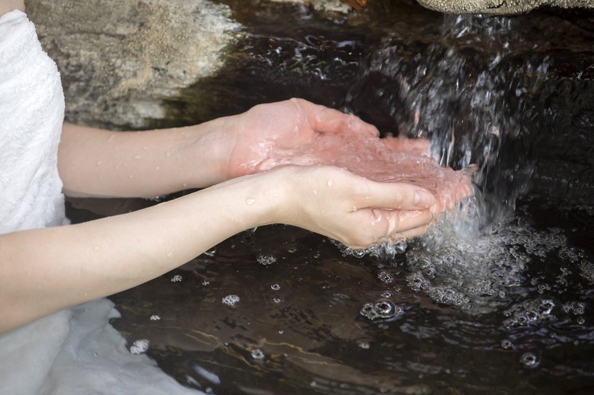 温泉の湯面に女性の手がやさしく触れている様子